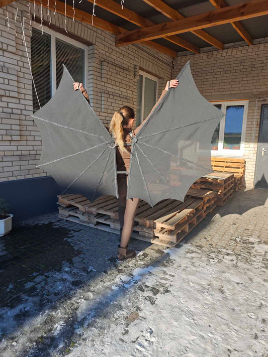 Person holding large gray bat wings on a construction site