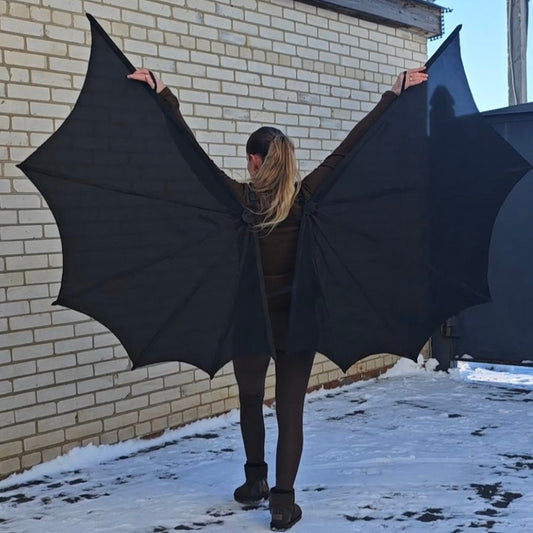 Person wearing large black bat wings outdoors on a snowy day.