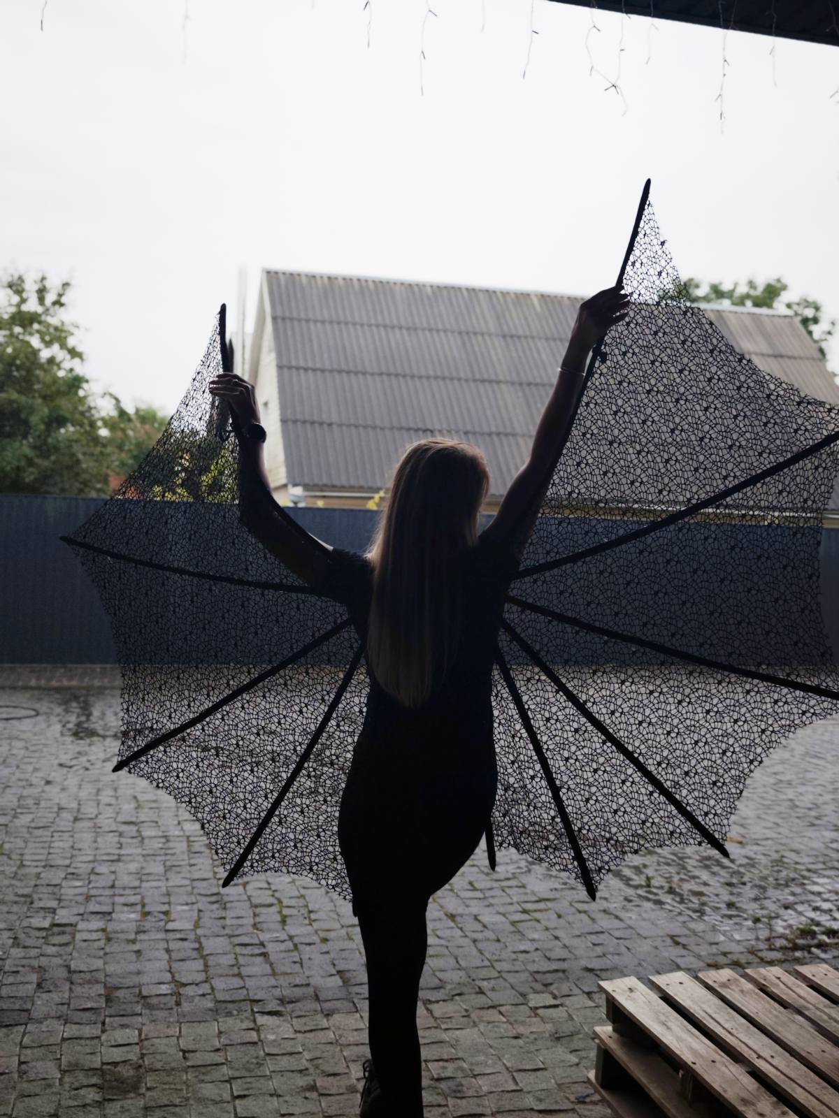 Person in large black bat lace wings outdoors on a rainy day.