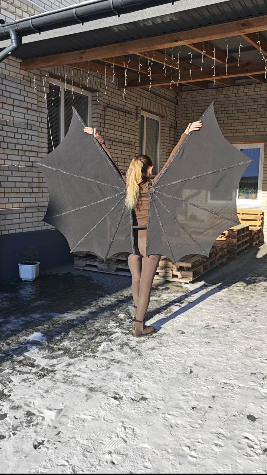 Person wearing handmade bay wings in front of a brick building with wooden pallets.
