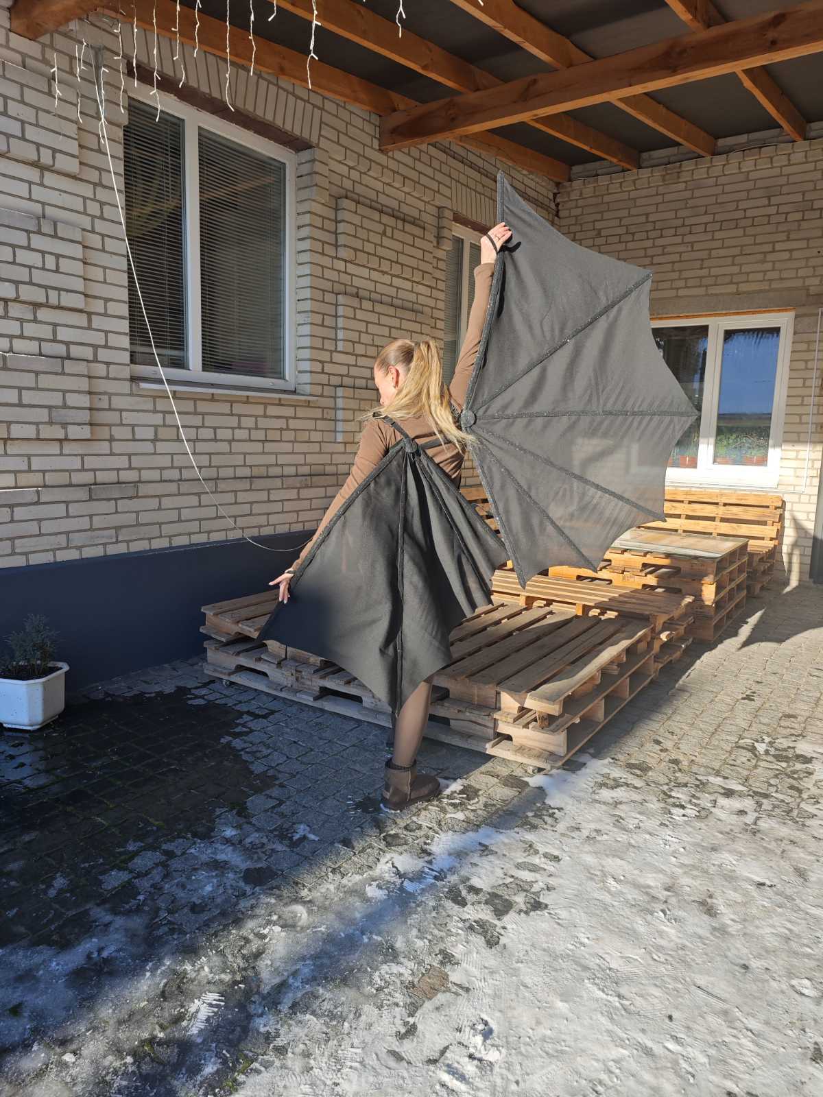 Person holding a large gray bat wings on a wooden pallet outside a building.