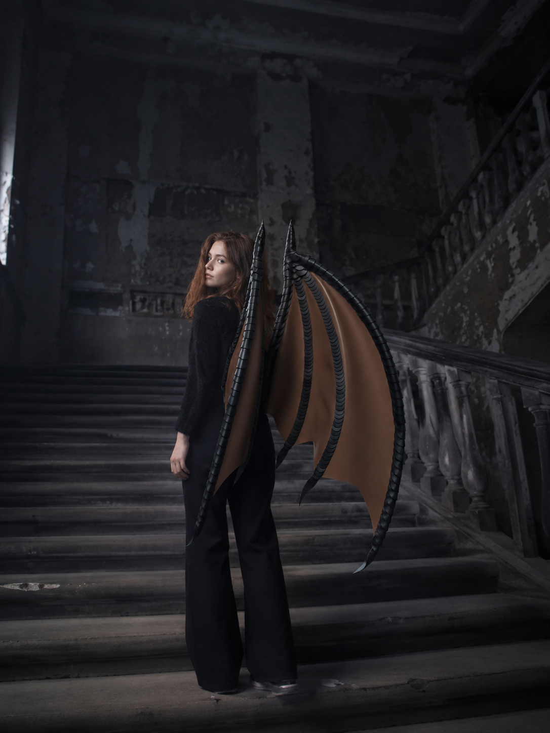 Person with large dragon-like wings standing on a dark staircase