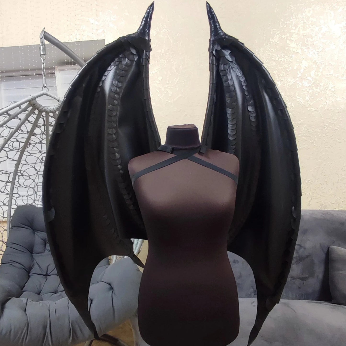 Mannequin with black wings on a stand in a room with gray furniture.