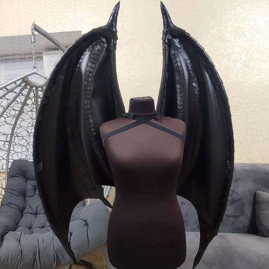 Mannequin with black wings on a stand in a room with gray furniture.