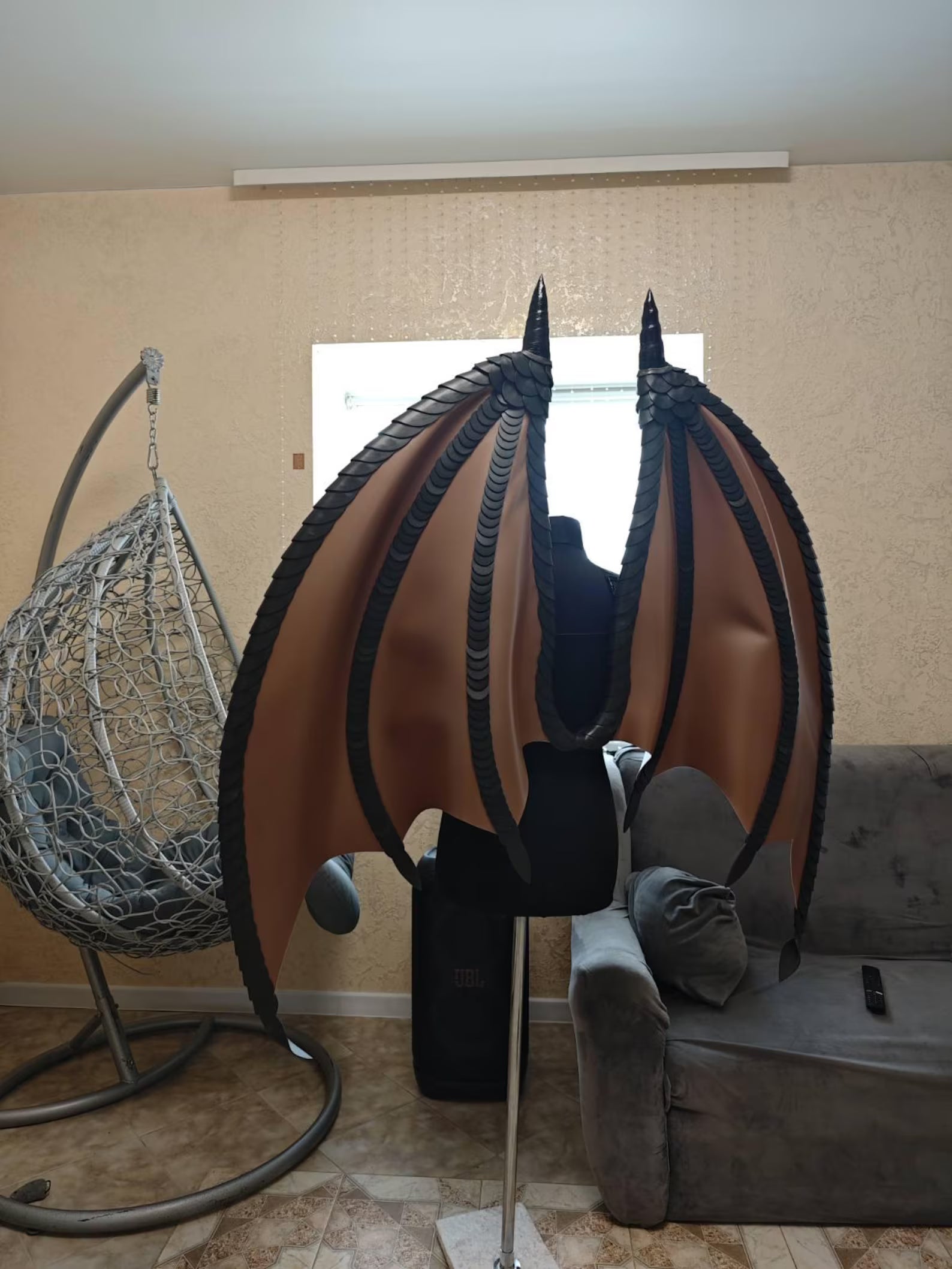 Mannequin with brown dragon wings in a room with a chair and sofa.