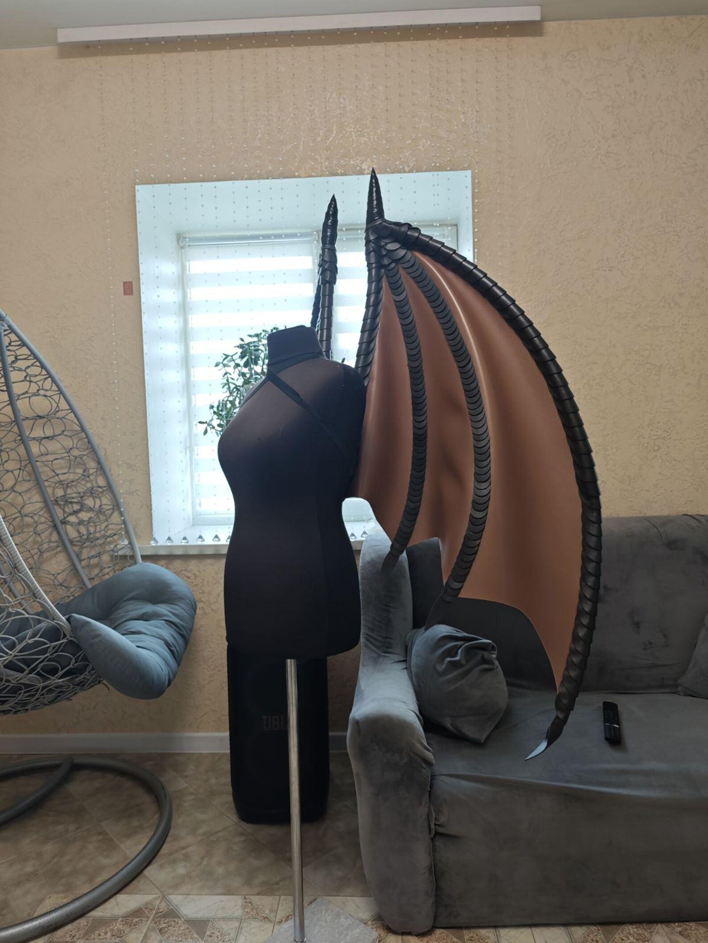 Mannequin with a black brown wings costume in a room with a gray chair, window, and plant.