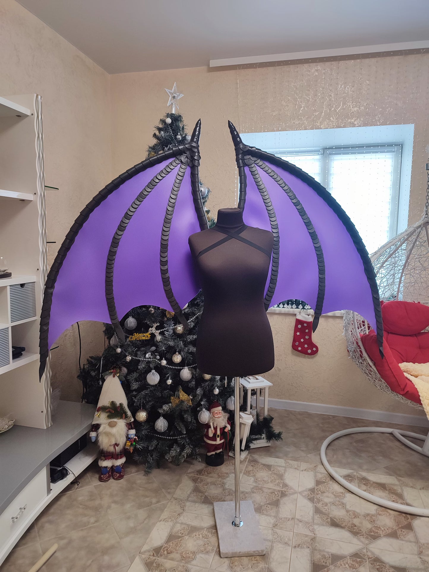 Mannequin with purple wings in a room with a decorated Christmas tree.