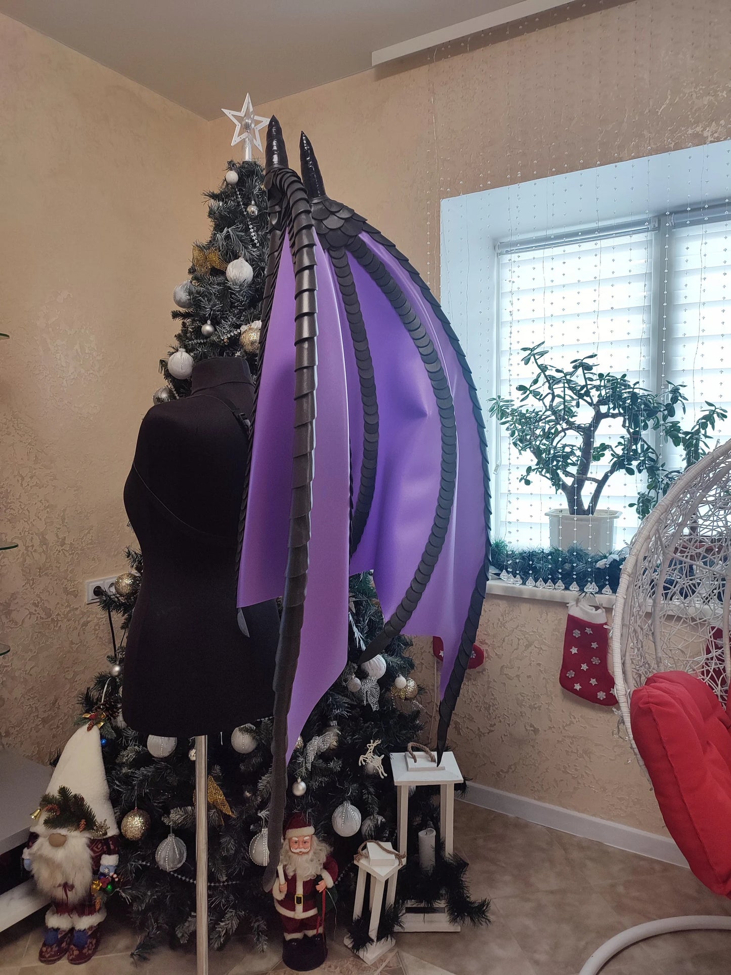 Mannequin with large purple and black wings in front of a decorated Christmas tree.