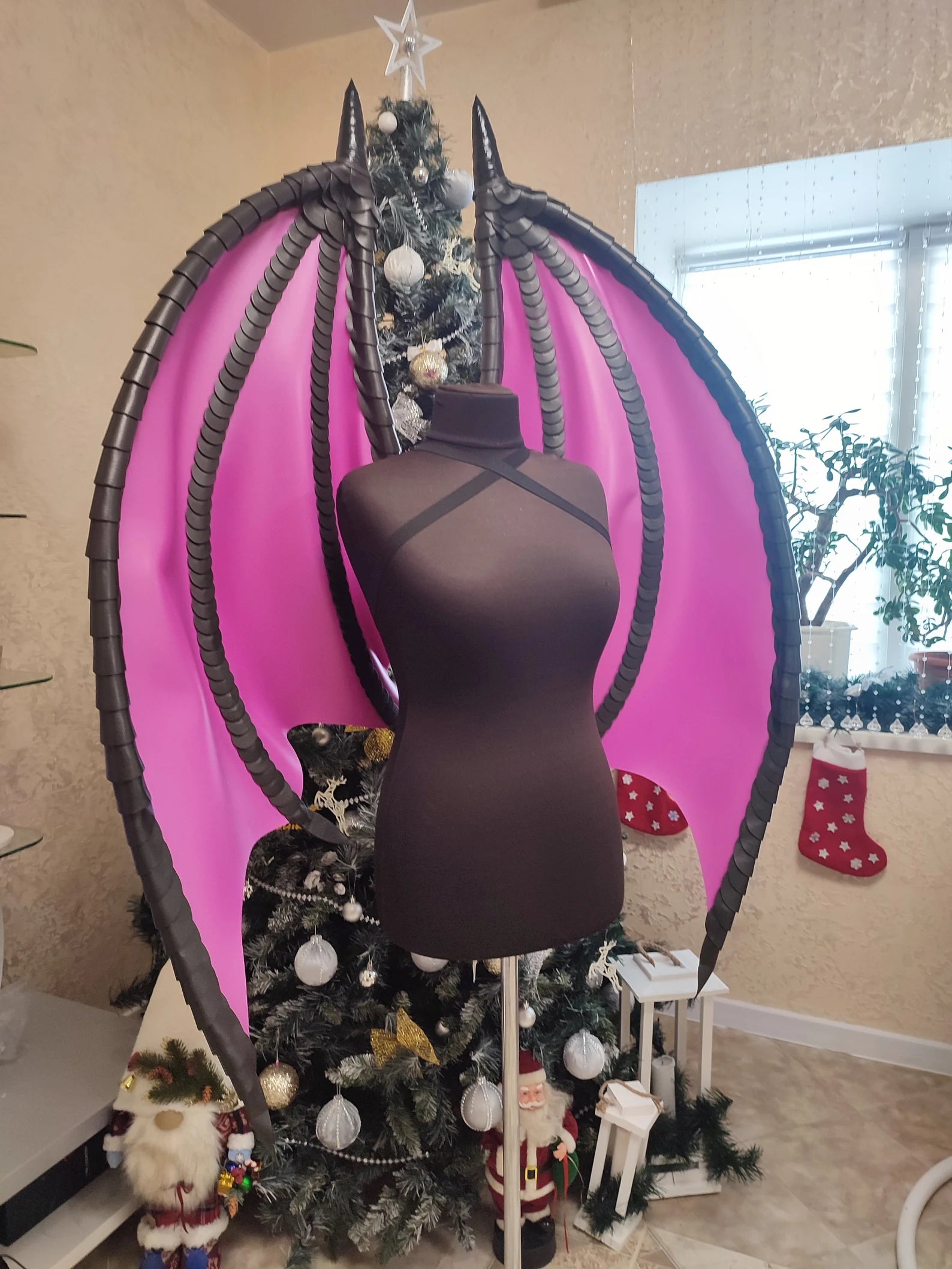Mannequin with pink and black wings in a room decorated for Christmas.