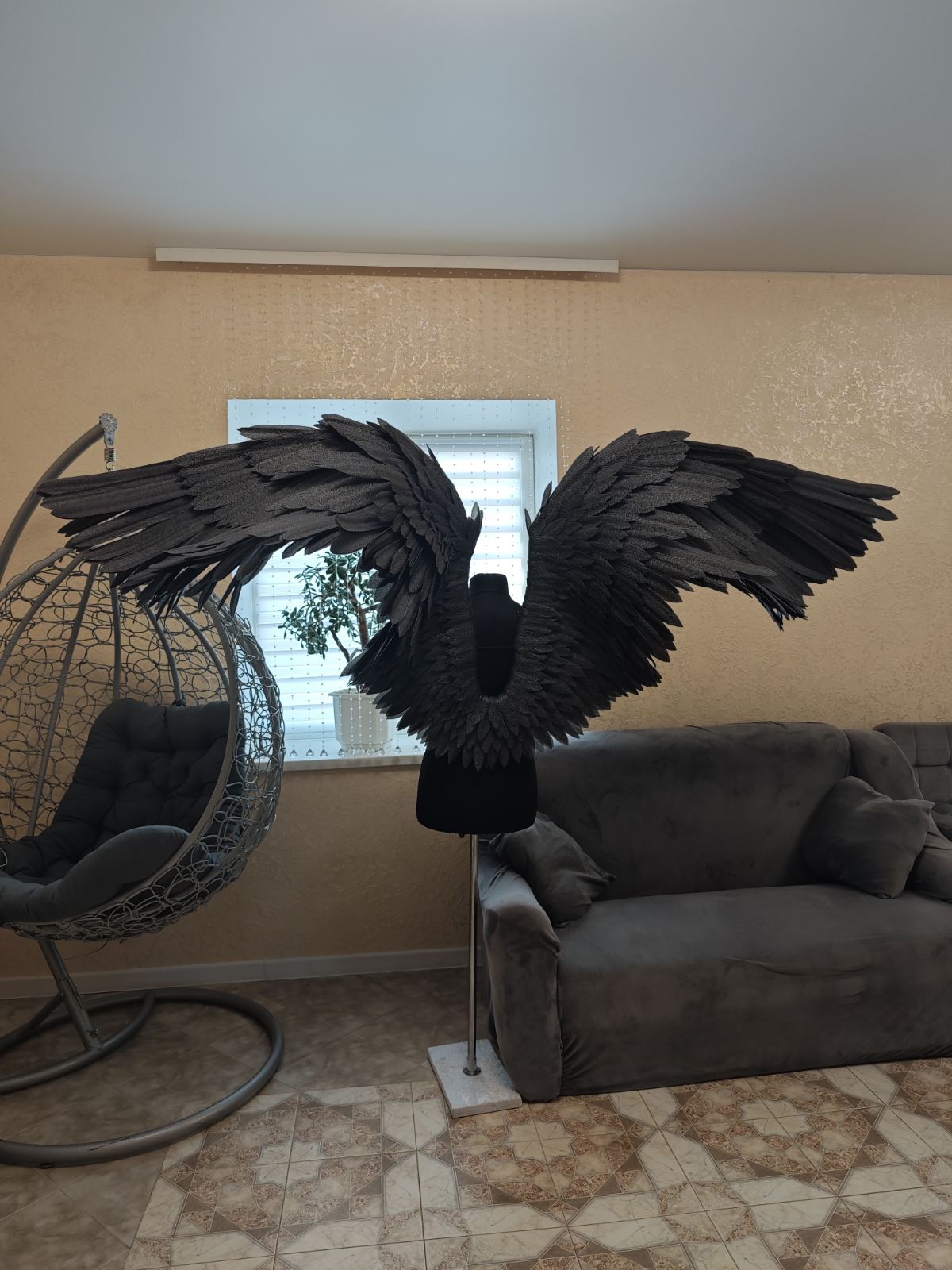 Black feathered wings on a stand in a living room setting with a couch and chair.