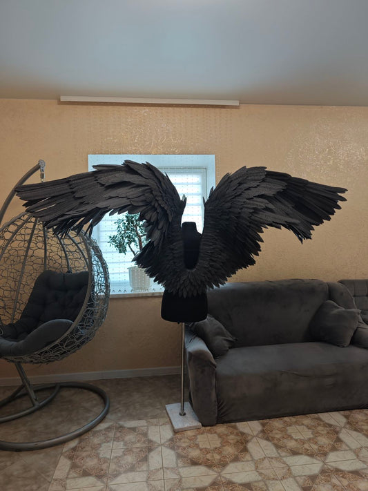 Black feathered wings on a stand in a living room setting with a couch and chair.