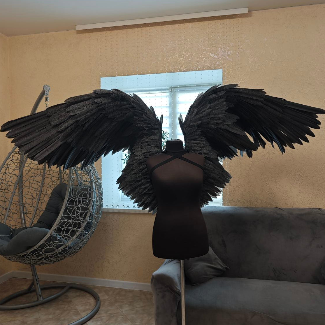 Black feathered wings on a mannequin in a living room setting with a couch and chair.