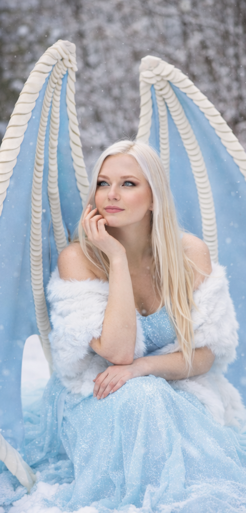 Woman in a blue dress with angel wings sitting on a snowy landscape