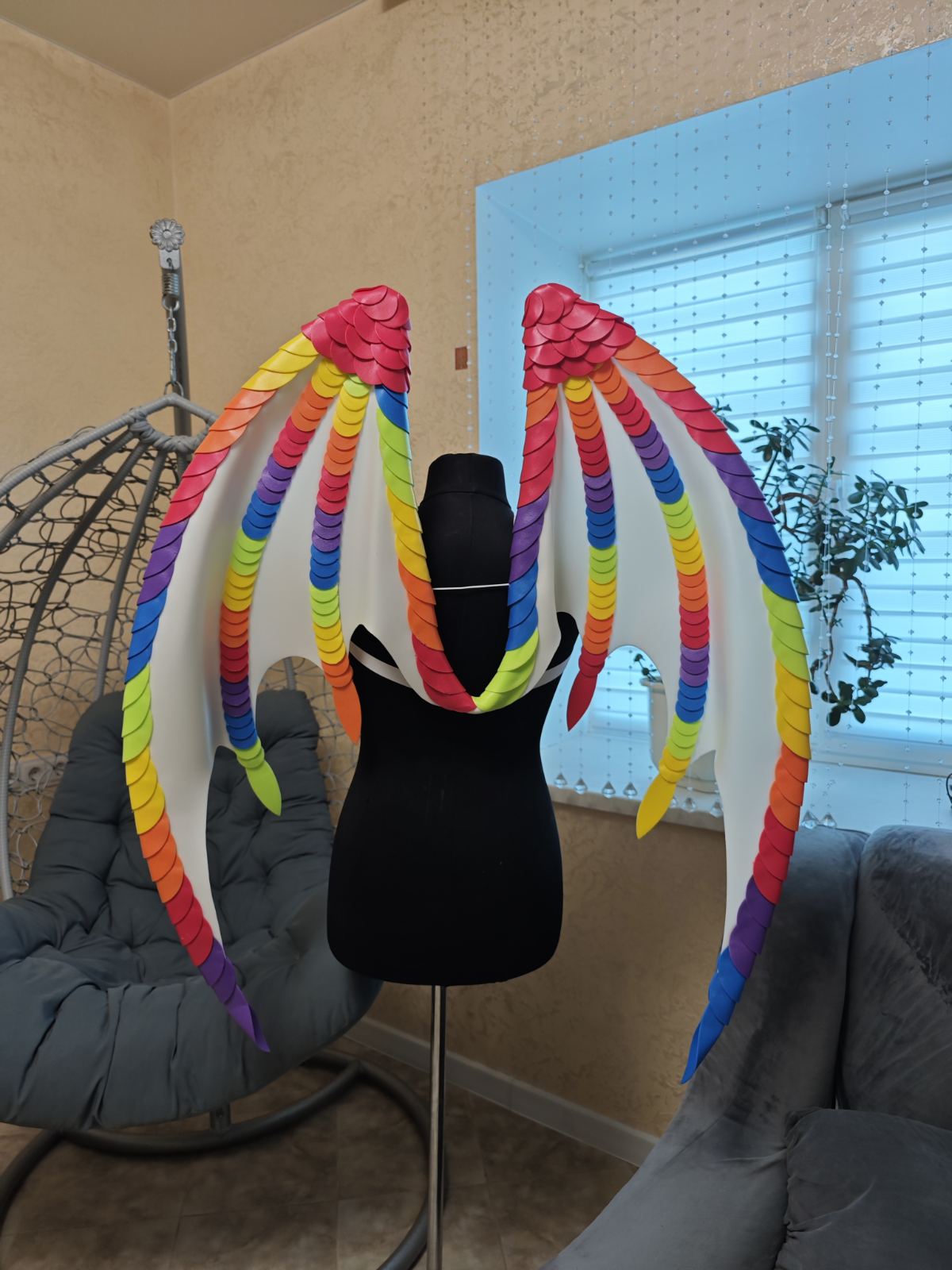 Mannequin head with colorful raqinbow wings in a room with a window and chair.