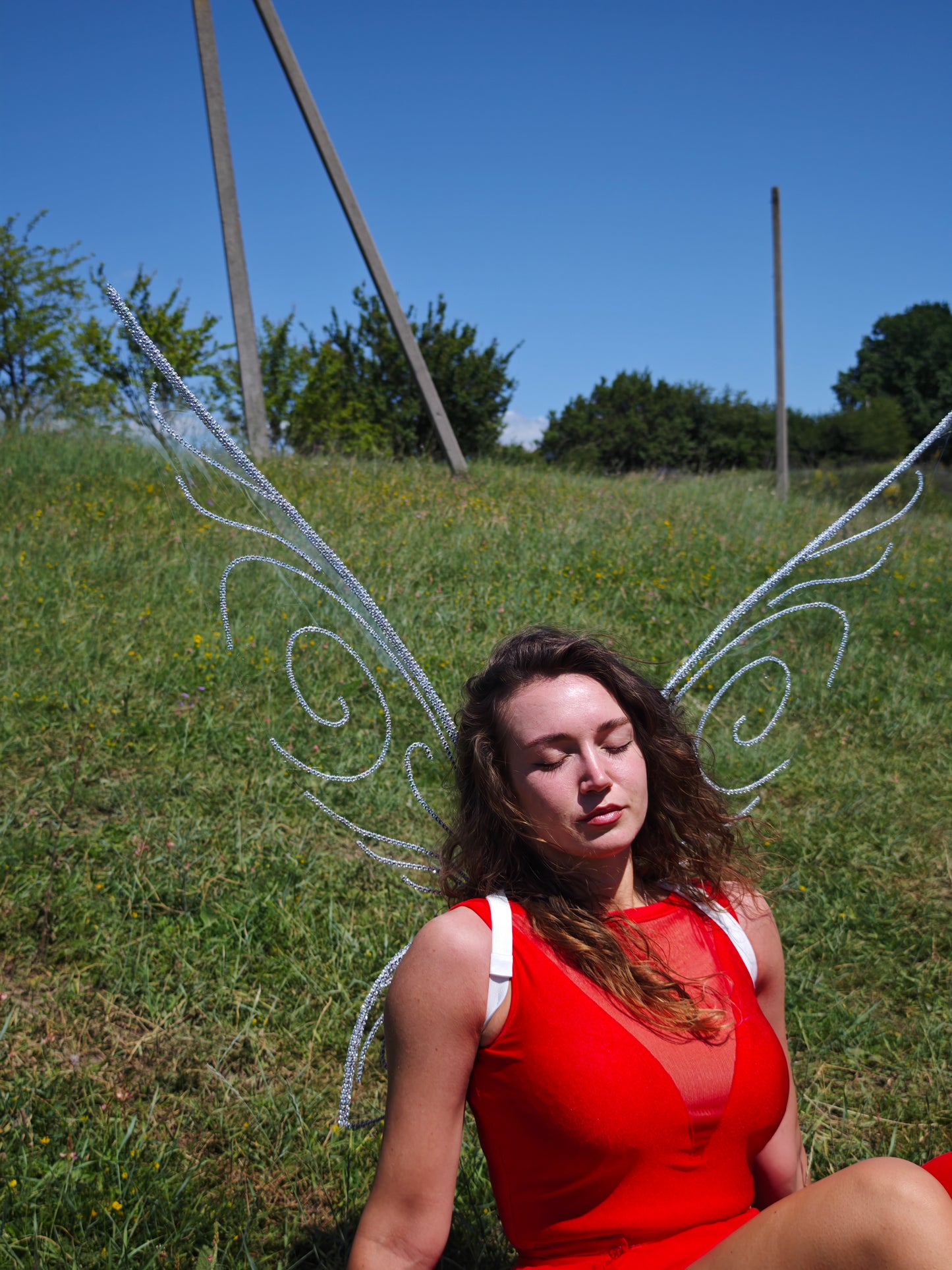 Woman in a red dress with fairy wings sitting on grass