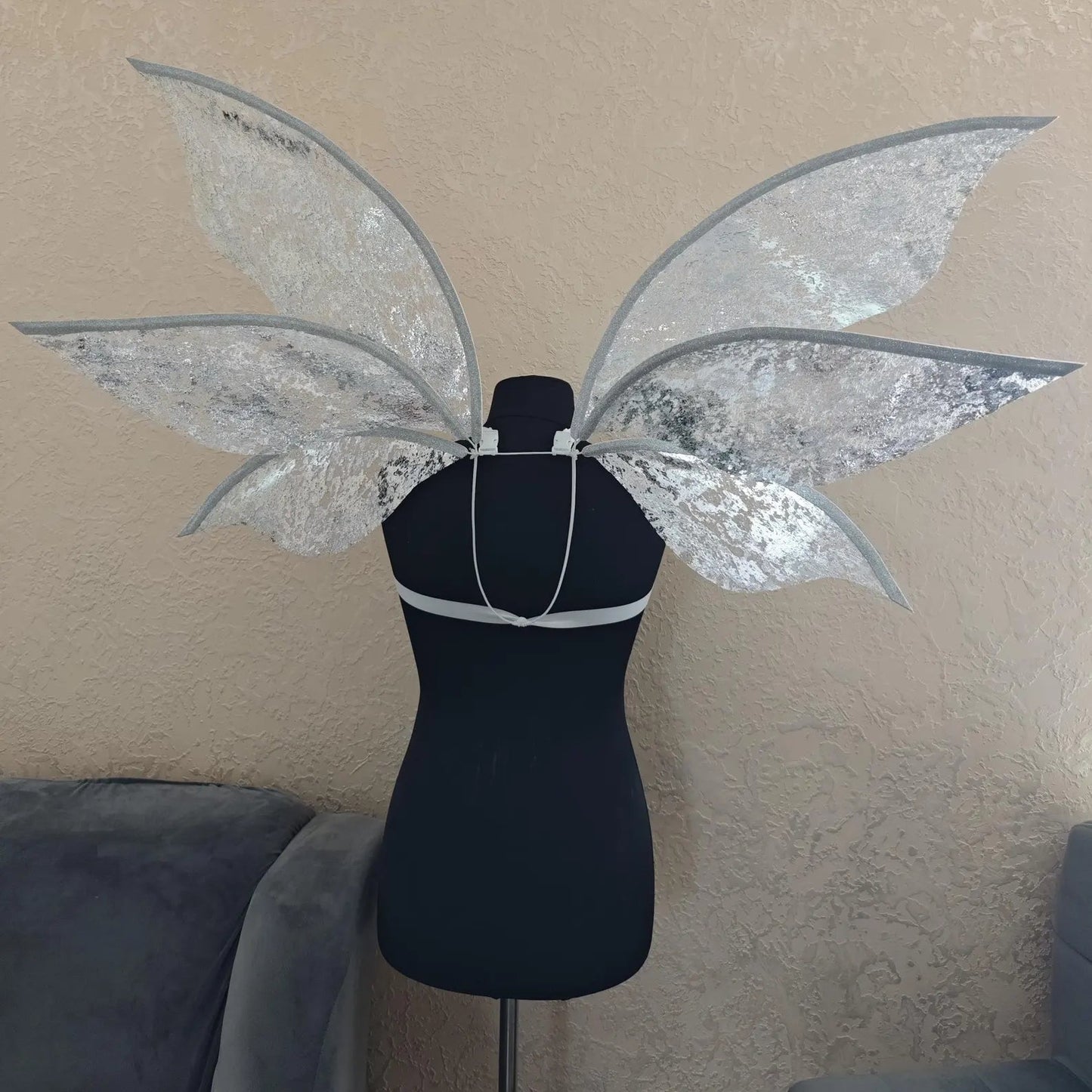 Silver fairy wings on a mannequin against a beige wall