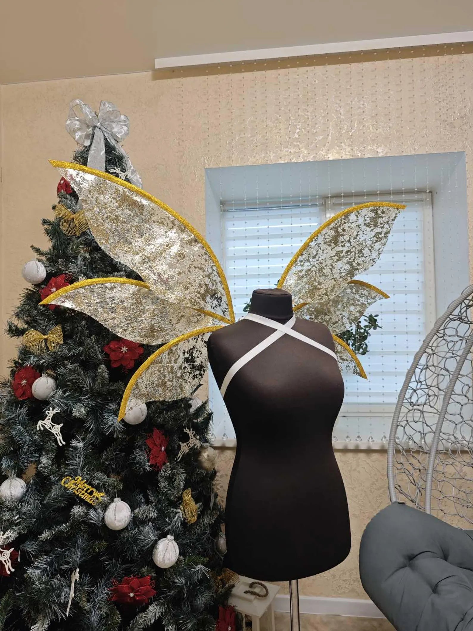 Decorated Christmas tree with large decorative wings and a mannequin with wings in a room.