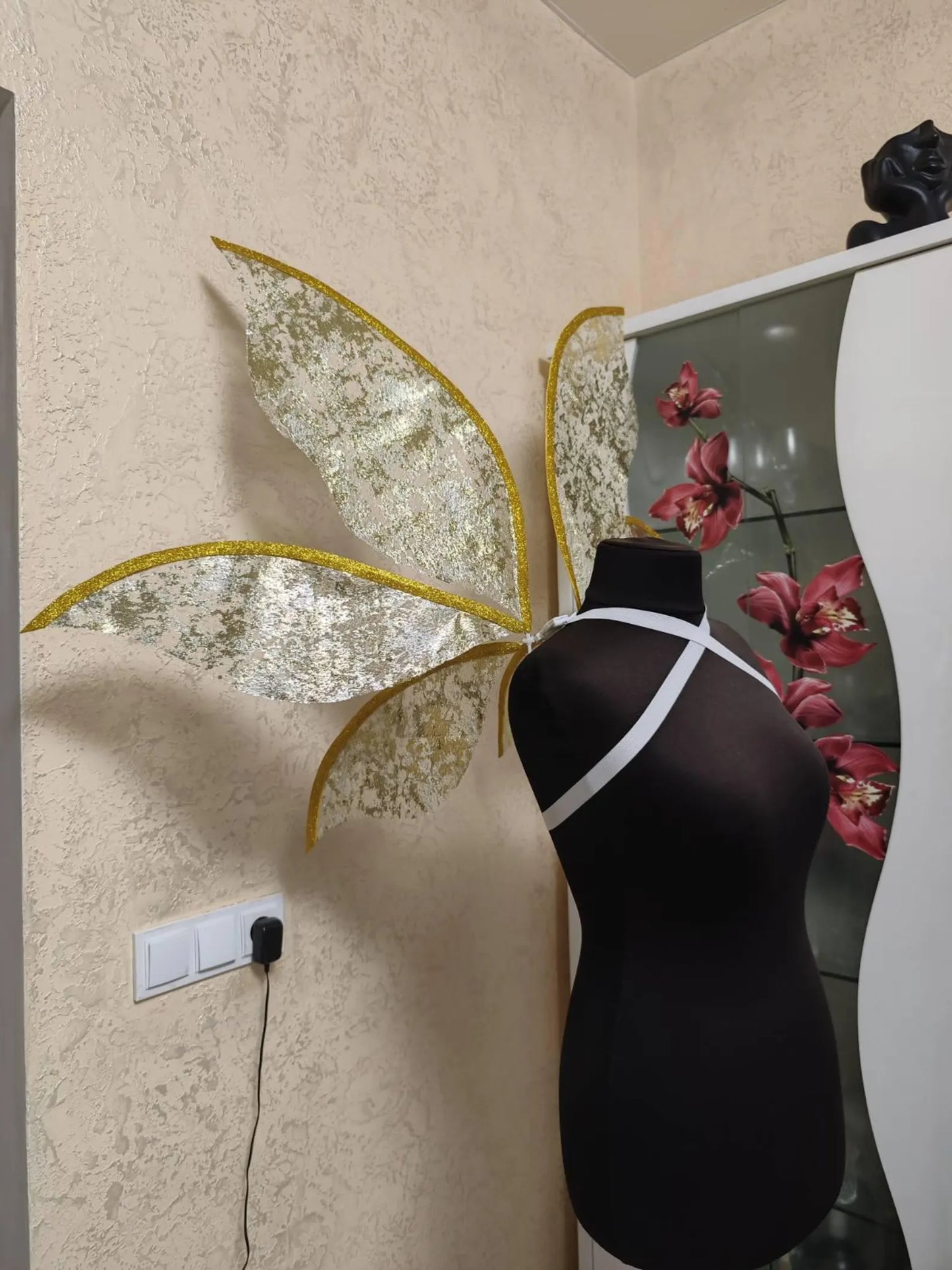 Mannequin with butterfly wings against a wall with decorative elements.