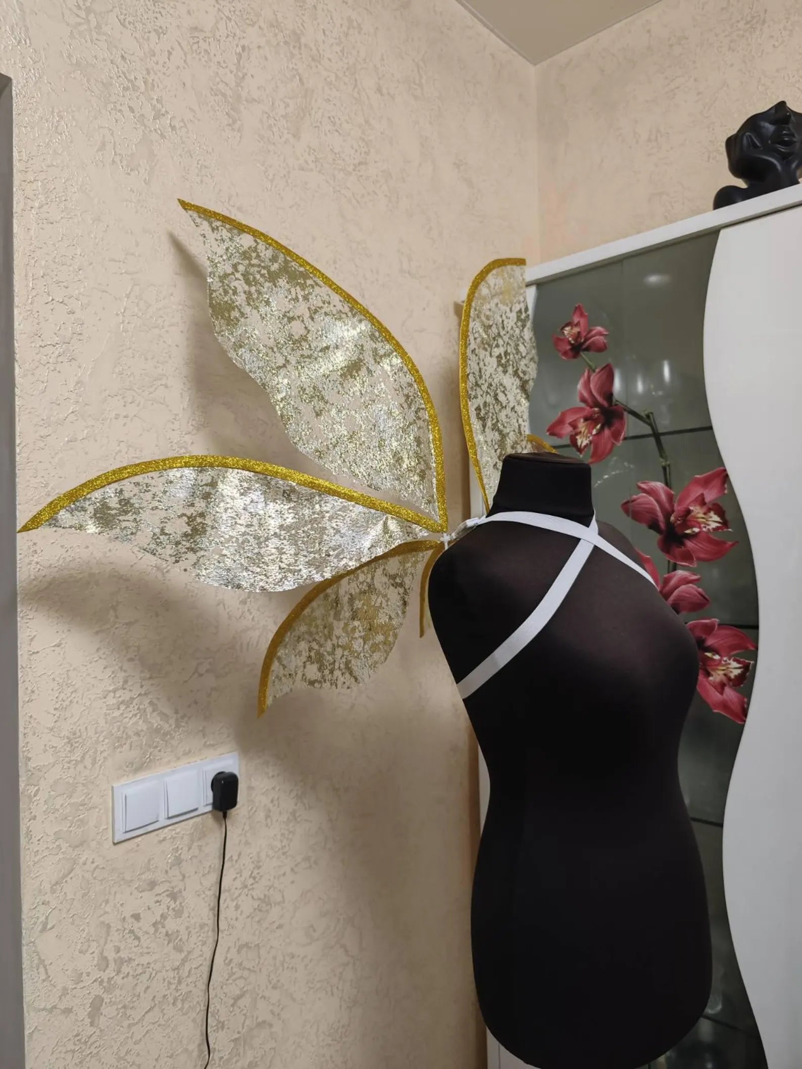 Mannequin with butterfly wings against a wall with decorative elements.