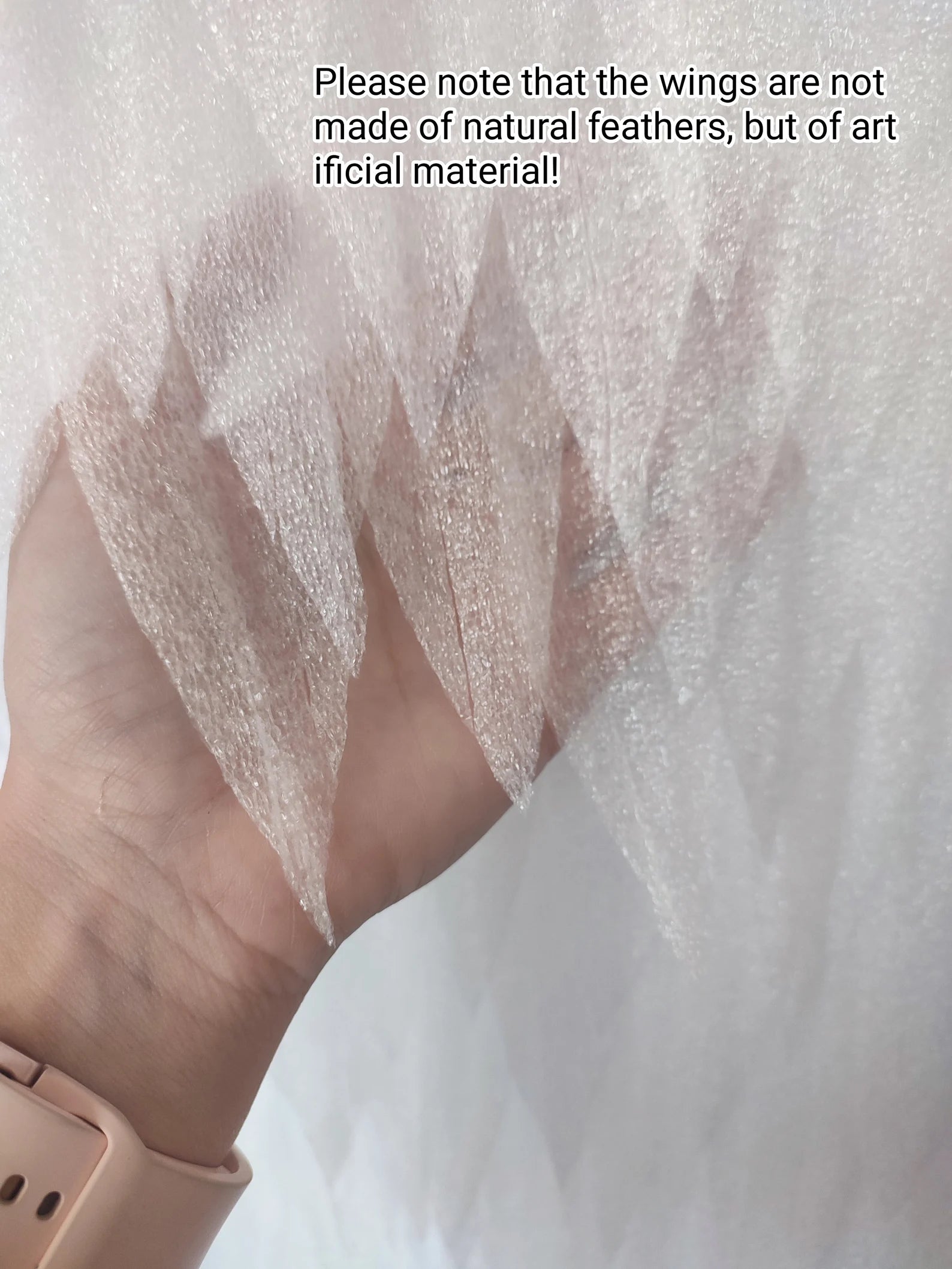 Close-up of a hand wearing sheer white wings with text indicating they are artificial.